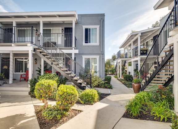 A row of townhouses with a concrete walkway and landscaping in the foreground.