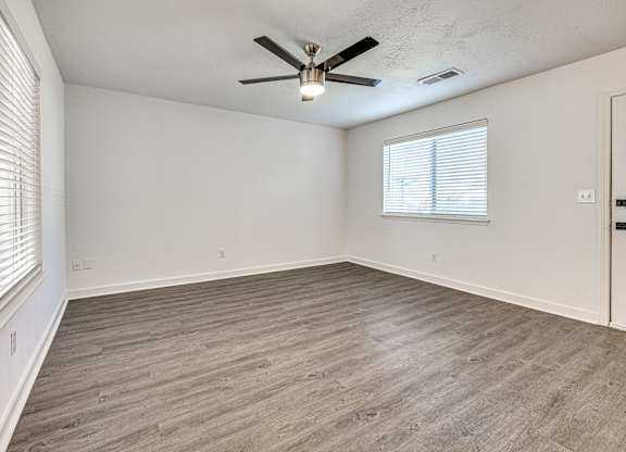 A room with a ceiling fan and light fixture, wooden flooring, and a window with blinds.