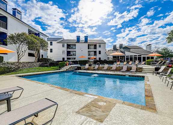 a swimming pool with lounge chairs and umbrellas in front of a building