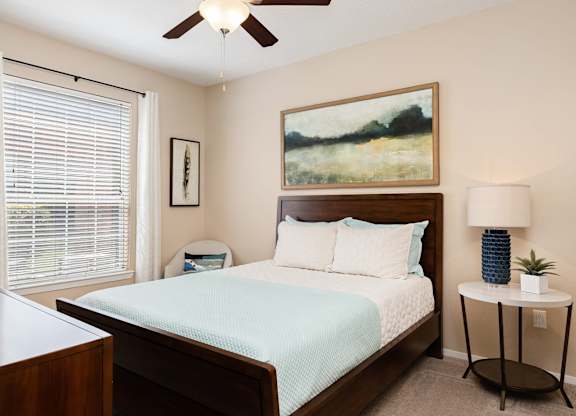 A bedroom with a bed, nightstand, and a painting on the wall.