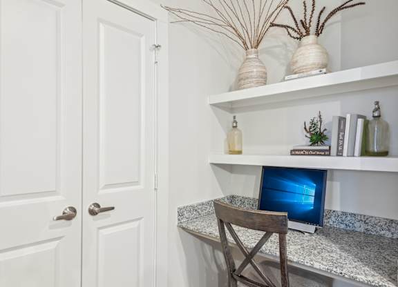 A white door is on the left and a desk with a laptop on it is on the right.