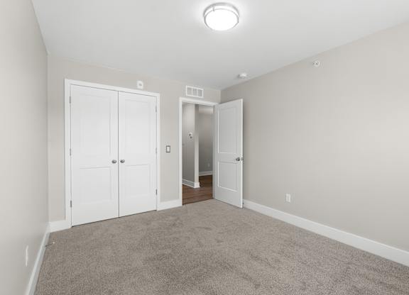 a bedroom with carpet and white doors and a door to a closet