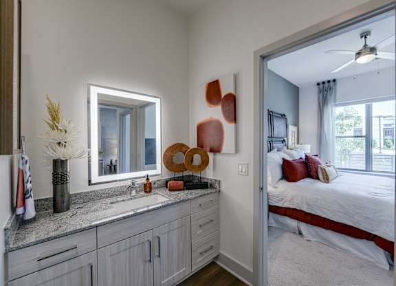 A bathroom with a large mirror and a bedroom in the background.