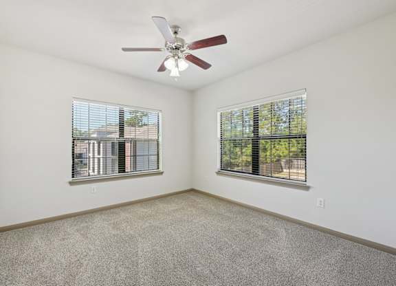 A room with a ceiling fan and two windows.