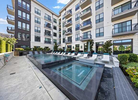 A large outdoor pool surrounded by lounge chairs and buildings.