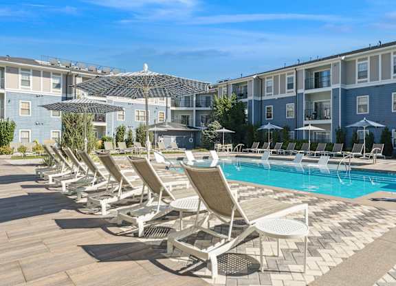 A row of sun loungers are set up by a pool.