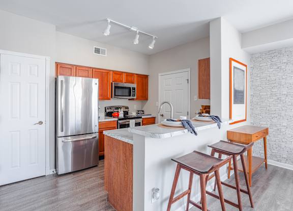 A kitchen with a white refrigerator, wooden cabinets, and a white island with two stools.