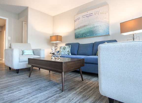 A living room with a blue couch, a white chair, and a wooden coffee table.