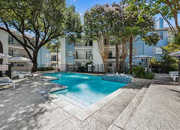 A pool surrounded by trees and apartment buildings.