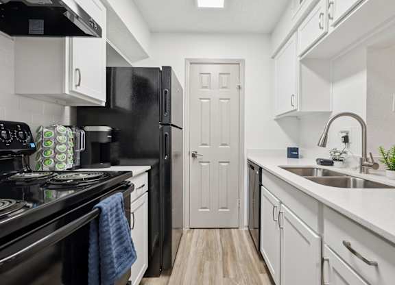 A black stove top oven sits next to a black refrigerator in a white kitchen.