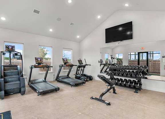 A spacious gym with treadmills, elliptical machines, and a bench press.