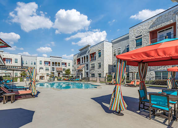 A pool area with a striped umbrella and chairs.