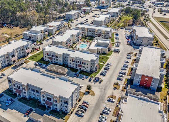 A bird's eye view of a residential area with multiple apartment buildings and cars parked in the parking lot.