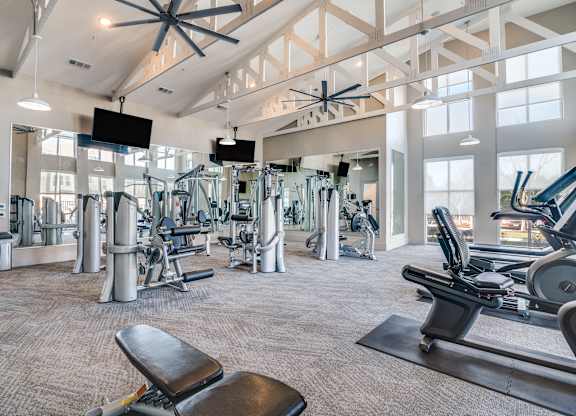A gym with a variety of equipment including treadmills, weights, and a bench.
