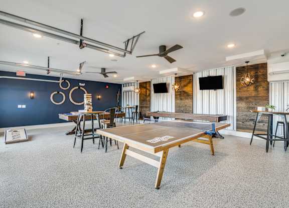 A ping pong table is in the middle of a room with a blue wall and a ceiling fan.