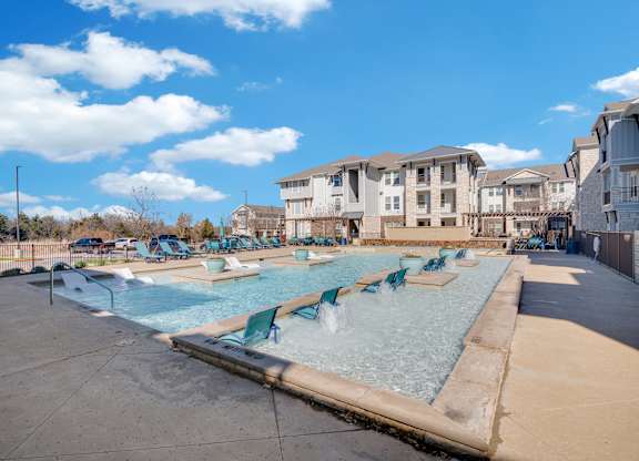 A swimming pool with chairs around it and apartment buildings in the background.