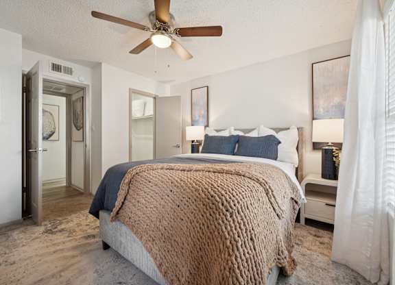 A bedroom with a bed covered in a brown blanket and a ceiling fan.
