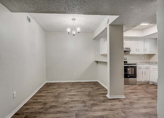 an empty living room with a kitchen in the background