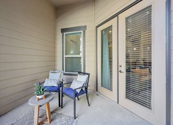 Private patio with beige siding featuring glass-framed French doors and a sliding casement window, furnished with an outdoor seating set.
