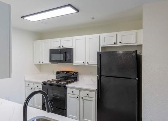 A black refrigerator sits in a kitchen with white cabinets and a black stove.