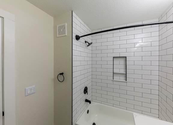 A white tiled shower with a white tub and a black shower head.