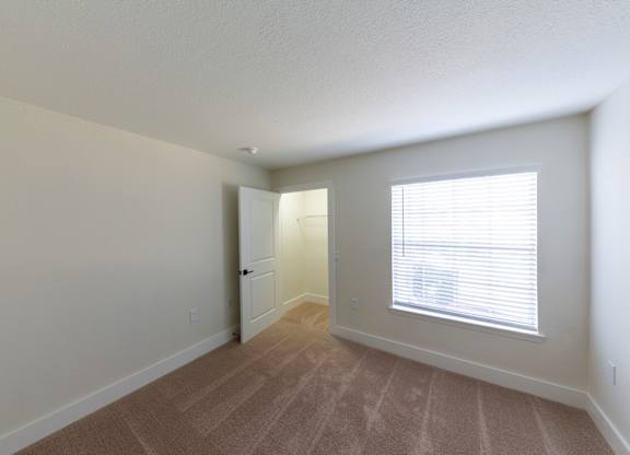 A room with a carpeted floor and a window with blinds.