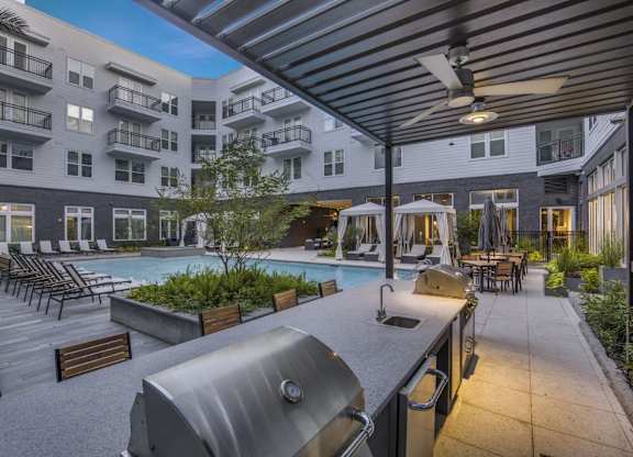 A modern outdoor kitchen area with a grill and a pool in the background.