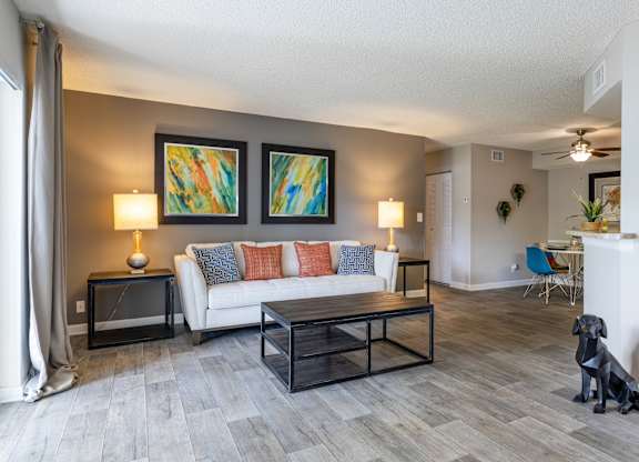 A living room with a white couch, a black dog, and two abstract paintings on the wall.