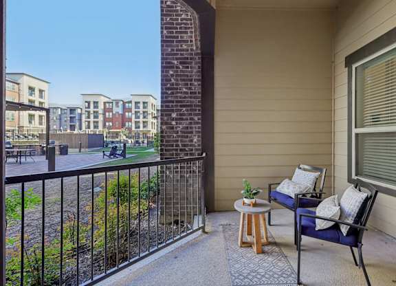 A balcony with a blue chair and a small table with a plant on it.