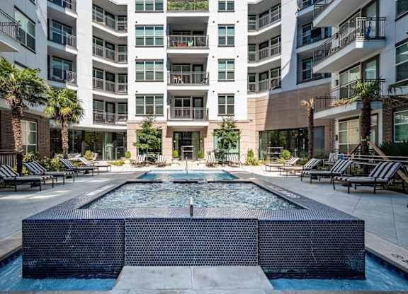 A large pool in the middle of a courtyard surrounded by lounge chairs and palm trees.