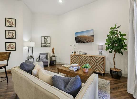 A spacious, open living room with expansive eggshell-colored walls and contrasting dark hardwood floors, brightly lit by natural light.