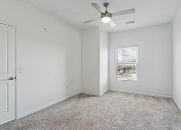A room with a ceiling fan and a window with blinds.
