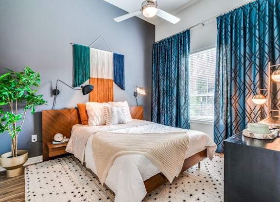 A bedroom with a bed, a potted plant, and a ceiling fan.