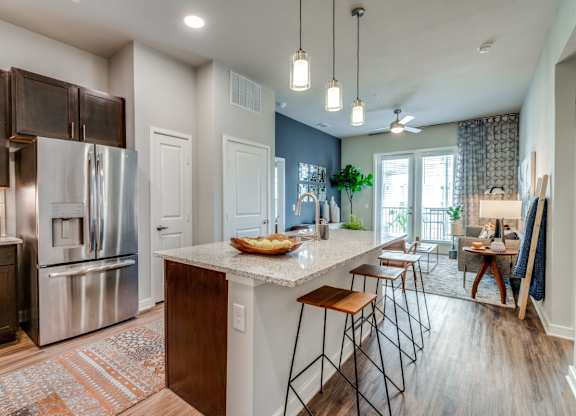 A kitchen with a refrigerator, stove, and bar stools.