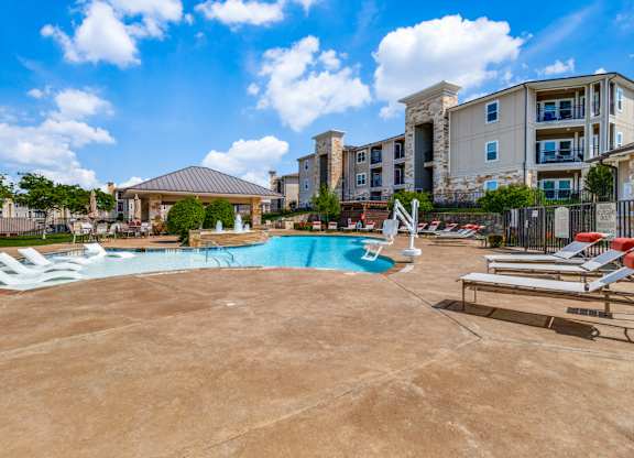 a resort style pool with lounge chairs and a building in the background