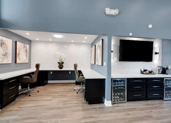 A modern home office with a desk, chairs, and a TV mounted on the wall.