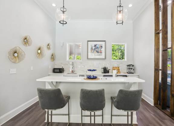 A white dining table with four grey chairs and a chandelier hangs above it.