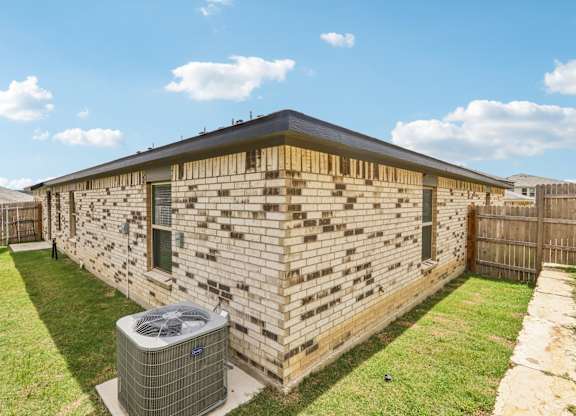 A house with a brown brick wall and a black roof with a fence and a green lawn.
