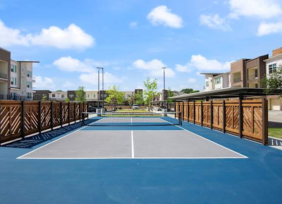 A tennis court is surrounded by apartment buildings.