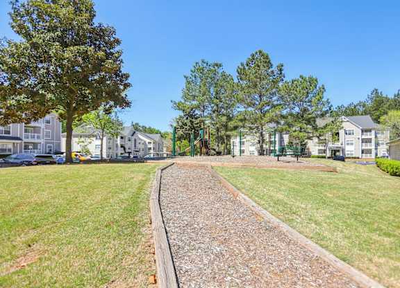 A gravel path leads through a grassy area with trees and houses in the background.