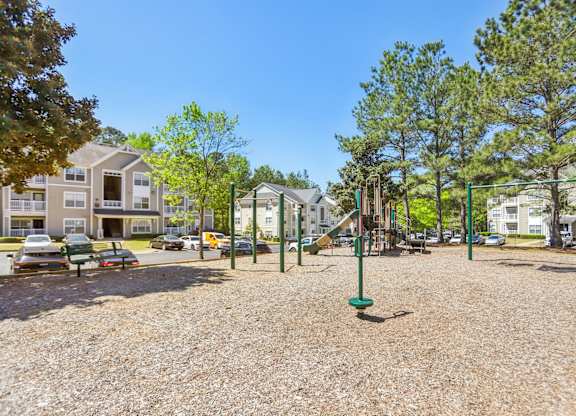A playground with a green pole in the middle of the gravel area.