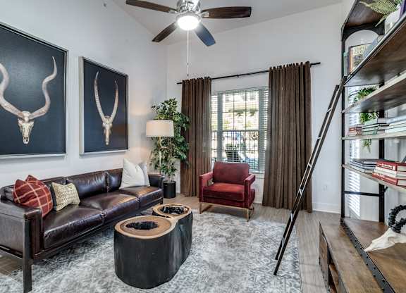 A living room with a black couch, a red chair, and two bull skulls on the wall.