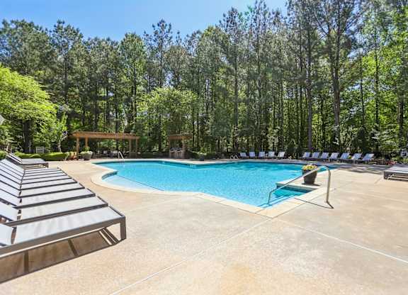 A pool surrounded by trees and lounge chairs.