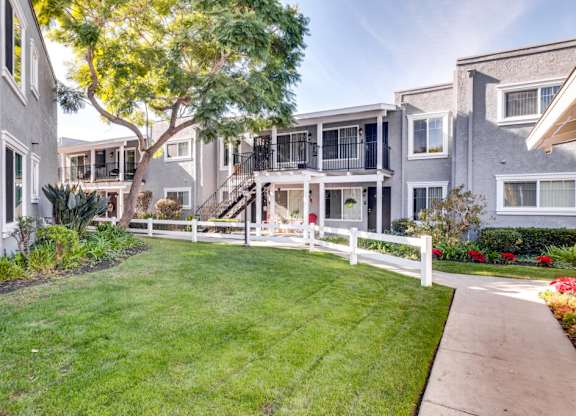 A well-maintained lawn leads to a white picket fence and a row of townhouses.