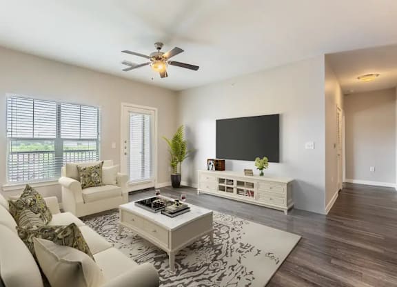 A living room with a white couch, a coffee table, and a flat screen TV mounted on the wall.