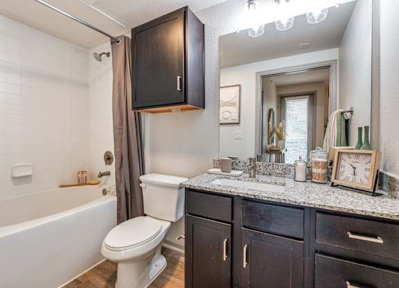A bathroom with a white toilet, a bathtub with a shower curtain, and a mirror above the sink.