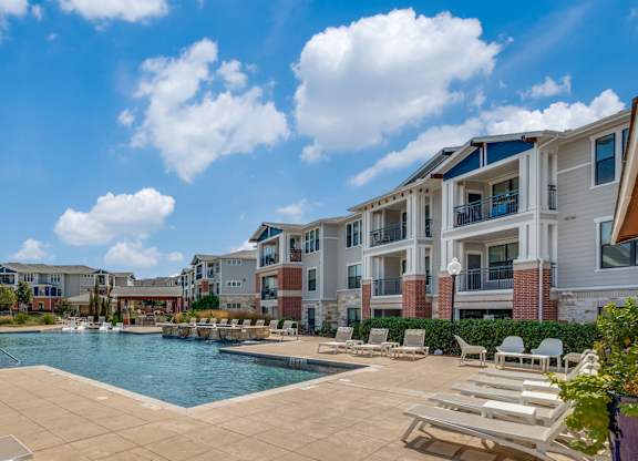 A pool surrounded by sun loungers and apartment buildings.