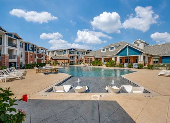 A large swimming pool surrounded by lounge chairs and buildings in the background.