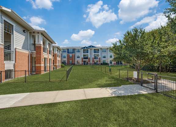 A row of apartment buildings with a black fence and green grass in front.