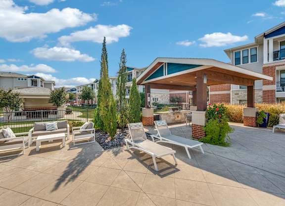 A patio with a couch, chairs, and a tree in front of a building.